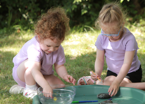Two girls playing outside with a water tray