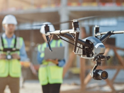 Two males in high visibility clothing flying drones