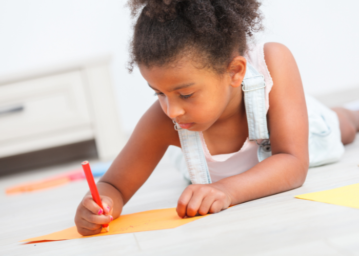 child lying on the floor whilst writing