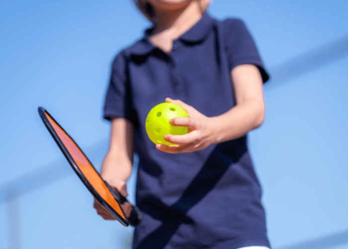 Child holding a pickleball paddle and ball