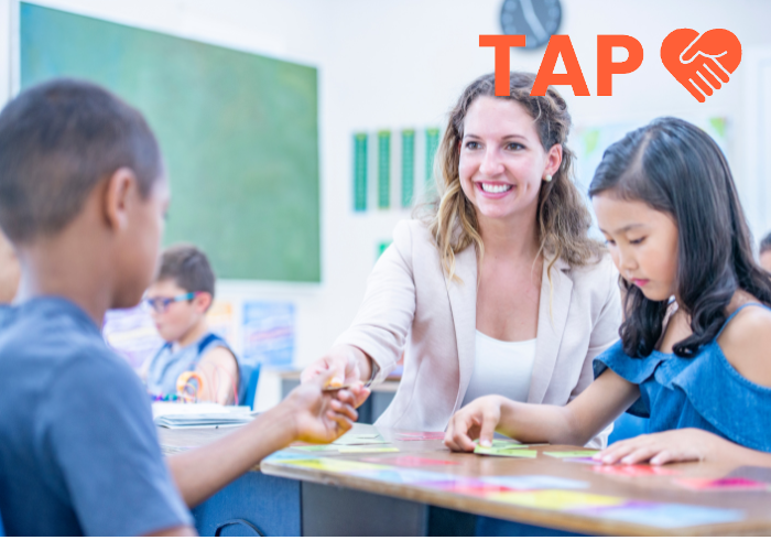 Smiling teacher sat with two pupils at a desk in a classroom