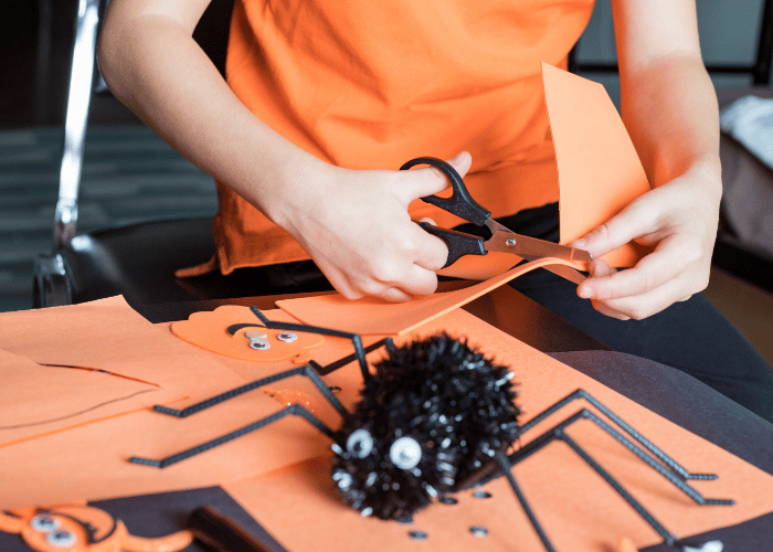 Person cutting orange paper next to craft spider