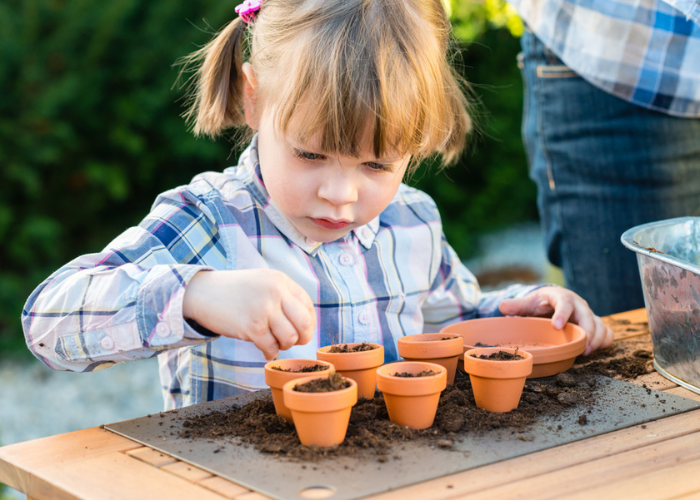 child putting soil into small plant pots